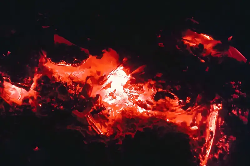 Lähikuva tasaisesti punaisena hehkuvasta hiilloksesta pimeässä, ei liekkejä.