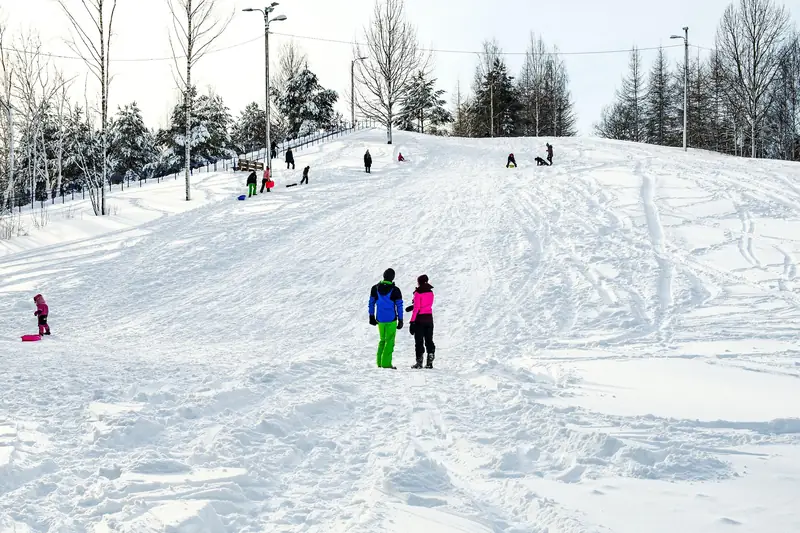 Leveä, tallattu pulkkamäki, jossa lapset laskevat ja aikuiset seisovat alhaalla.